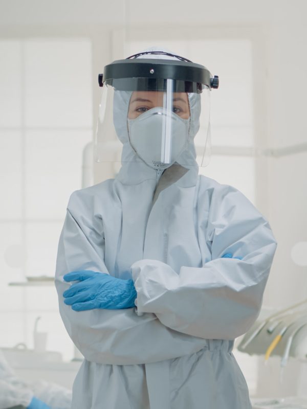 Portrait of dentist standing in hazmat suit for virus protection at oral clinic. Caucasian woman wearing coverall ppe prepared for dentistry operation and surgical consultation